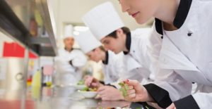 a row of potential chefs taste their dishes in a culinary school