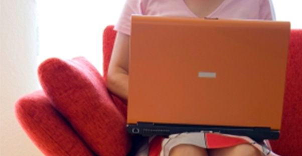 a woman sits on her couch and explores online mba options on her laptop