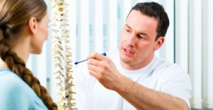 a doctor points to a spine model and explains ankylosing spondylitis to a patient