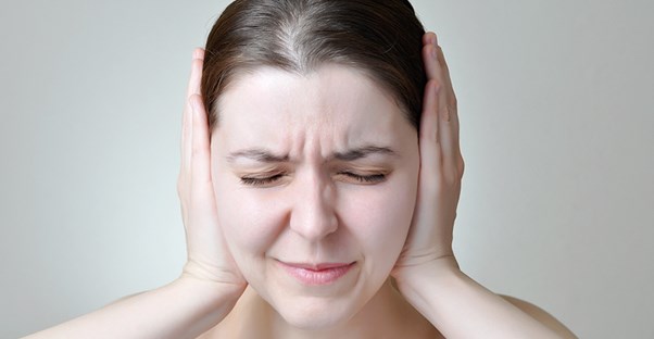 a woman holds her ears to symbolize hearing loss