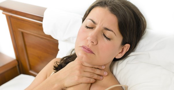 a woman in bed holds her throat due to heartburn